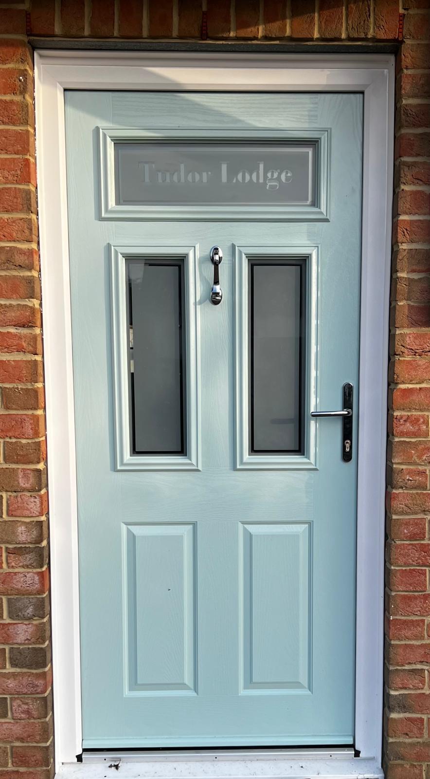 Light blue composite front door with etched glass and chrome hardware in a brick surround